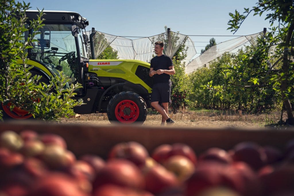 Man leaning on CLAAS NEXOS admiring orchard