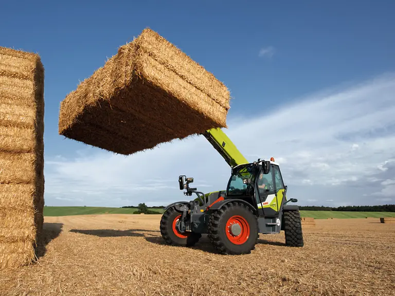 CLAAS Scorpion Telehandler lifting bales in a harvested field