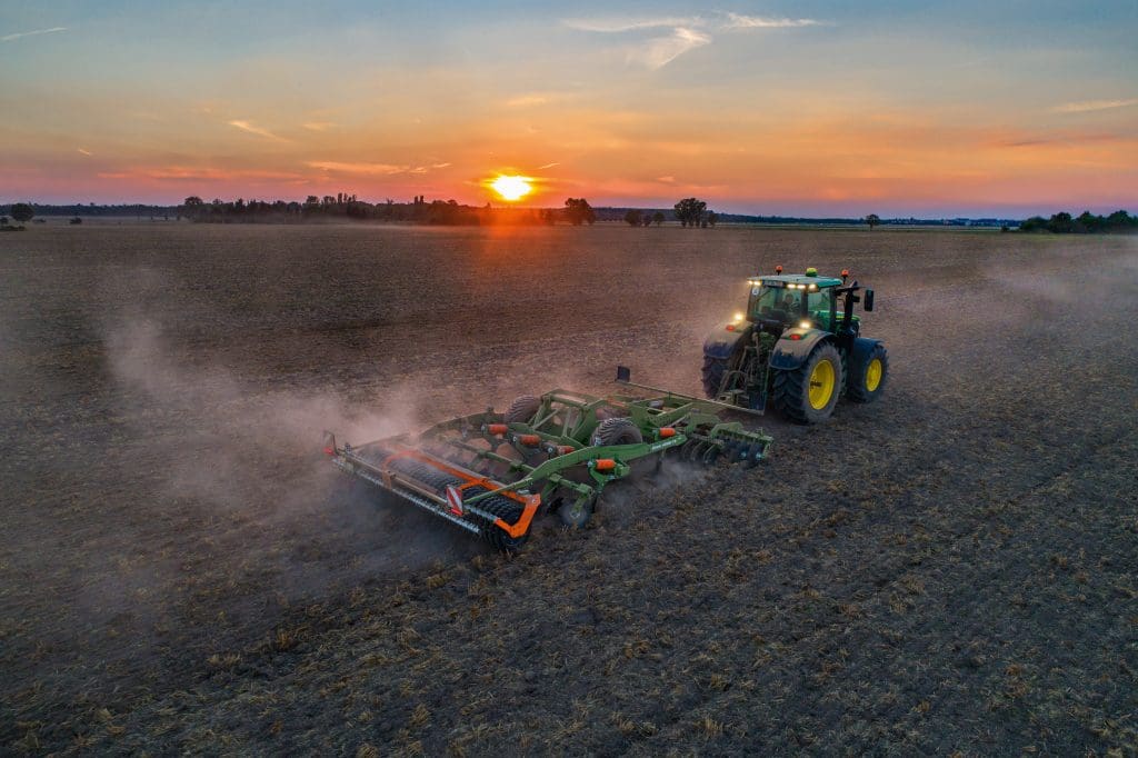 Tractor pulling an amazone ceus cultivator in field at sunset